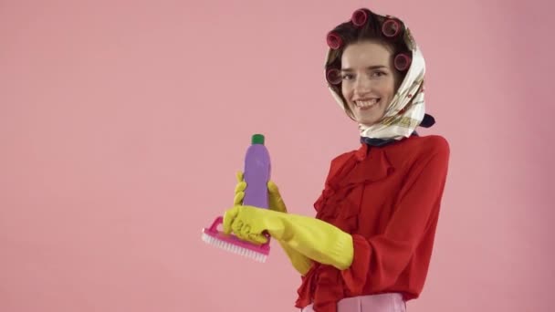 A woman in a blouse and hair curlers brushes her hair with a pink brush, smiles. — Stock Video