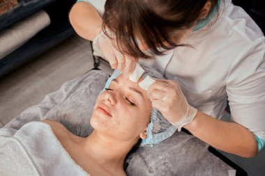 Genç bir kadın kozmetikçi müşterilerin yüzlerindeki sivilceleri mekanik olarak temizler..