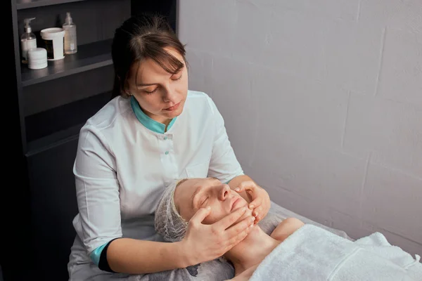 Uma cosmetologista feminina faz uma massagem facial em um salão de beleza. — Fotografia de Stock