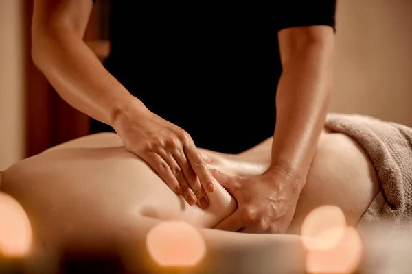 Uma mulher gosta de uma massagem nas costas com óleo em um salão de beleza. Luz de velas. — Fotografia de Stock