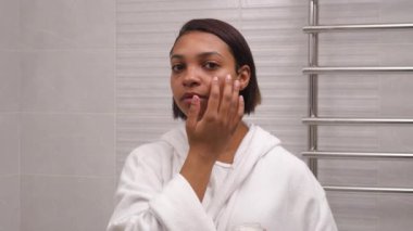Koyu tenli güzel bir kadın yüz nemlendirici kullanır. Spa günü.