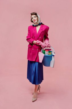 Ceketli ve etekli bir kadın elinde bir kova temizlik malzemesi tutuyor..