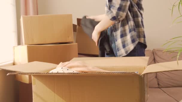 Ekose gömlekli bir kadın karton bir kutudan giysilerini çıkarıyor.. — Stok video