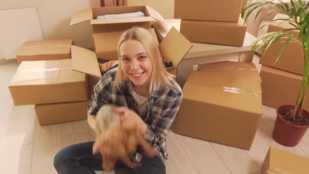 Uma mulher senta-se no chão e abraça o seu cachorrinho. Muitas caixas de papelão. — Vídeo de Stock