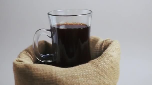 El vigorizante café en una taza de vidrio se encuentra en una bolsa de arpillera, gira en su lugar. — Vídeos de Stock