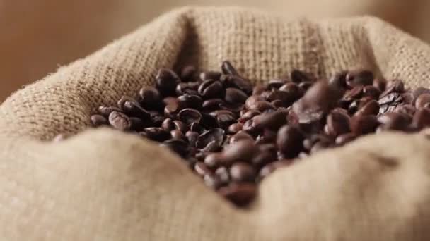 Close-up of dark coffee beans falling from above into an eco-friendly burlap bag — Stock Video