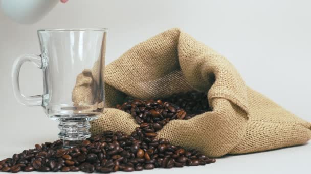 Pour fresh brewed coffee into a clear mug. A burlap bag with coffee beans. — Stock Video
