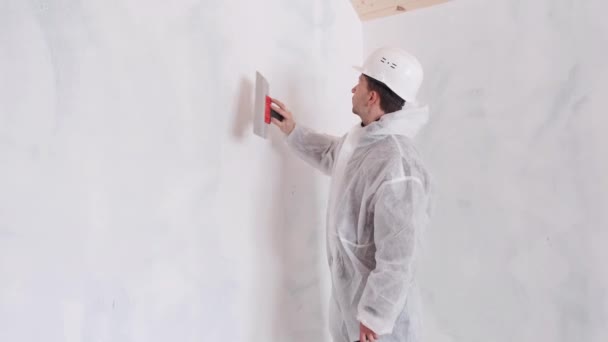 Un homme en combinaison de protection applique du mastic sur les murs pour aligner les murs. — Video