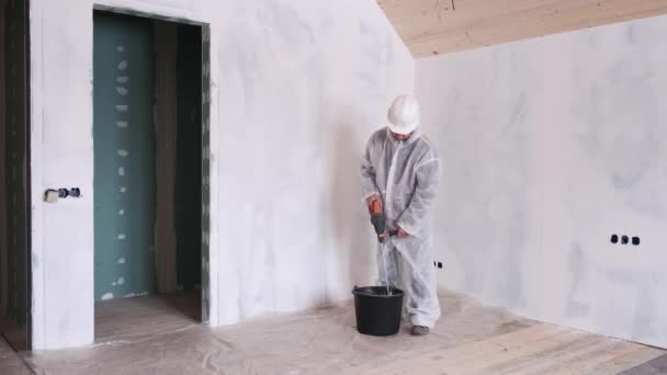 A man in a protective suit and a hard hat mixes cement for repairs in houses. — Stockvideo