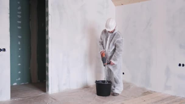 Un homme en costume de protection et chapeau dur prépare le ciment pour les réparations de la maison. — Video
