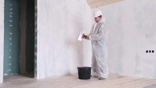Homem com uma espátula em suas mãos e um terno protetor faz reparos na casa — Vídeo de Stock