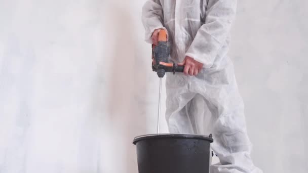 Vue latérale d'un homme mélangeant du ciment dans un seau noir. Costume de protection. — Video