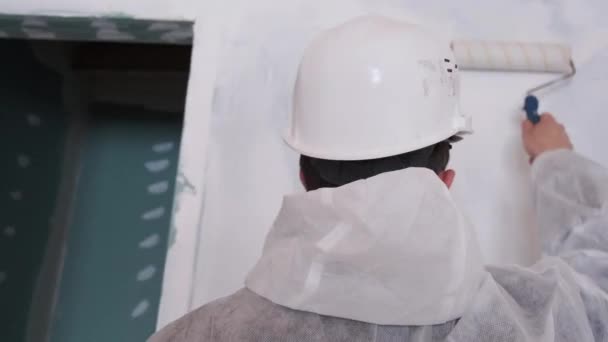 En vy från baksidan av en man som målar väggarna med vit färg. — Stockvideo
