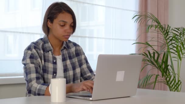 Egy fiatal nő, aki laptopot használ, online tanul otthon. Kényelmes munkahelyi környezet — Stock videók