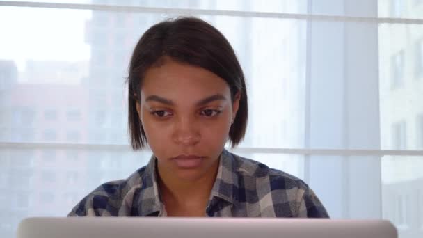 Uma mulher negra sentada em casa a olhar para um monitor de computador portátil. Trabalho e estudo online — Vídeo de Stock