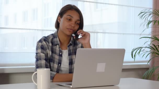 Woman using a laptop, working online at home. Communicates on the phone, takes — ストック動画