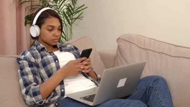 Μια γυναίκα που χρησιμοποιεί ένα ασημί φορητό υπολογιστή και smartphone ενώ βρίσκεται στον καναπέ. — Αρχείο Βίντεο