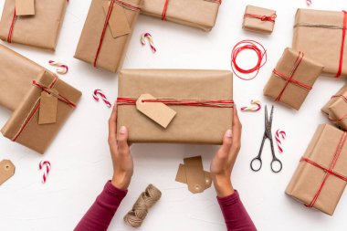 Kadının elleri, kraft kağıdıyla süslenmiş Noel hediyesi kutusunu tutuyor.