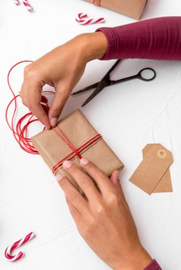 Bir bayanın elleri kraft kağıdıyla süslenmiş Noel hediyesi kutularını paketliyor.