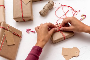 Bir bayanın elleri kraft kağıdıyla süslenmiş Noel hediyesi kutularını paketliyor.