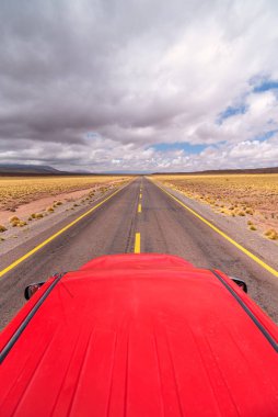Atacama Çölü, Şili 'de bulutlu bir günde asfalt yolda giden kırmızı araba.