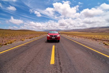 Atacama Çölü, Şili 'de bulutlu bir günde asfalt yolda giden kırmızı araba.