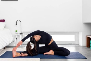 Genç, sıska kadın evdeki modern minimalist yatak odasında yoga yapıyor.