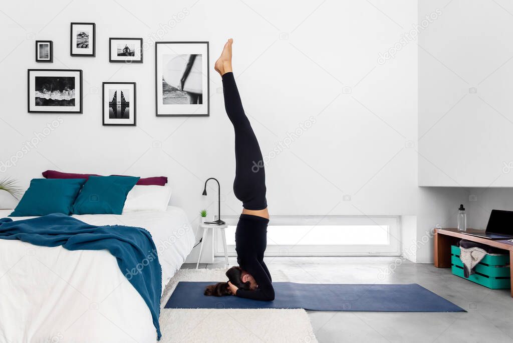 Fit woman practicing a headstand exercise, (salamba sirsasana pose) at her cozy home