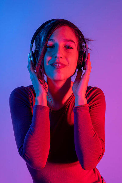 Привлекательная женщина с наушниками слушает музыку в студии с синим и красным огнями