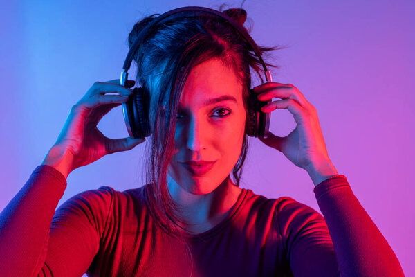 Привлекательная женщина с наушниками слушает музыку в студии с синим и красным огнями