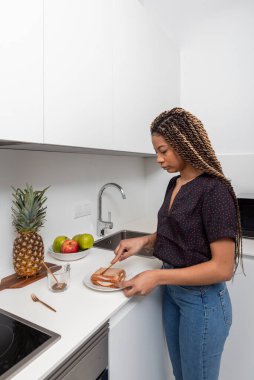 Hafif modern ev mutfağında kahvaltıya sağlıklı sandviçler hazırlayan genç bir kadının yan görüntüsü.