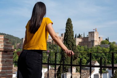 Back view of female tourist standing on terrace and admiring Alhambra fortress in Granada, Spain