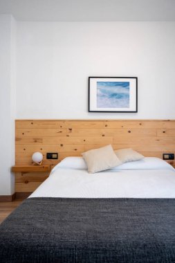 Işıl ışıl beyaz yatak odasının içi, deniz dalgaları ve ahşap bir yatak başlığıyla süslenmiş.
