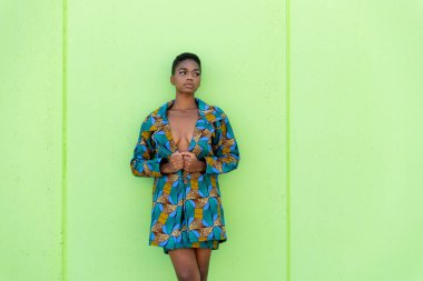 Geleneksel Afrika kumaşlı genç siyahi kadın fıstıklı arka plana bakıyor.