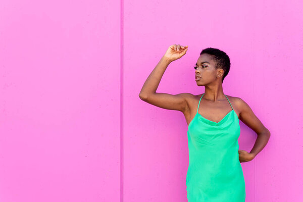 Young black female with green outfit and arms over head against pink background