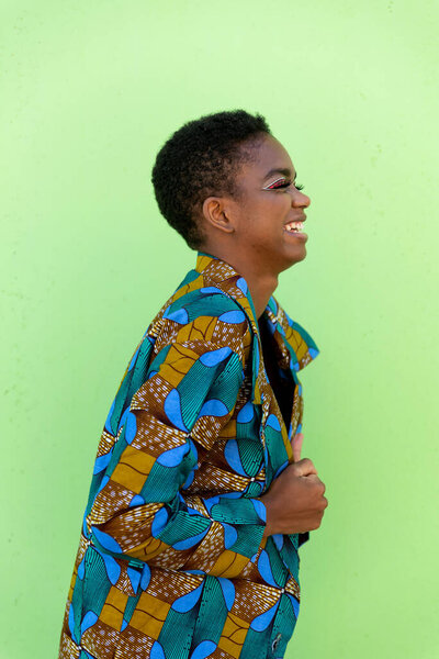 Young black female in traditional African piece of fabric smiling against pistachio background
