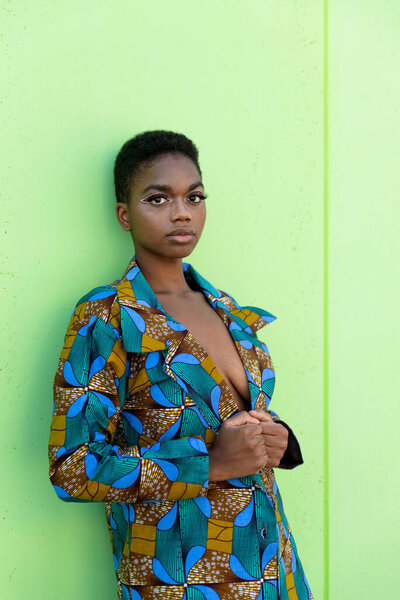 Young black female in traditional African piece of fabric looking at camera against pistachio background