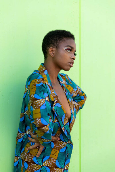Young black female in traditional African piece of fabric looking away against pistachio background