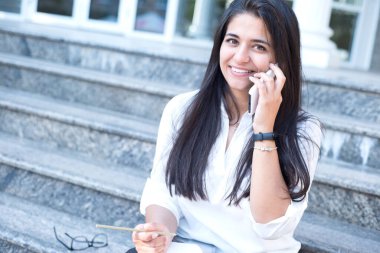 Güzel bir Hintli kızın portresi. İş kadını ofis binasının girişinde merdivenlerde oturuyor. Kız telefonda gülüyor ve konuşuyor.