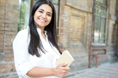 Genç ve güzel bir Hintli kızın portresi. Beyaz gömlekli bir iş kadını elinde bir not defteri tutuyor. Eski bir ofis binasının arka planında dikiliyorum.