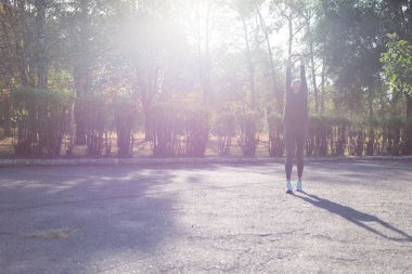 Sporcu kadın parkta ısınıyor. Şehir genci, güzel bir yaz gününde şehirde koşmadan önce ısınıyor.