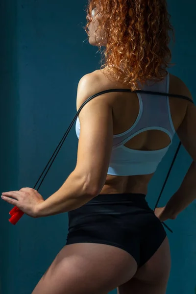完璧な筋肉や運動体を持つアスリートの女の子 スキップロープを保持します テクスチャブルーの壁の背景に対してポーズ美しいスポーツの女の子は ロープをジャンプして演習を行います — ストック写真