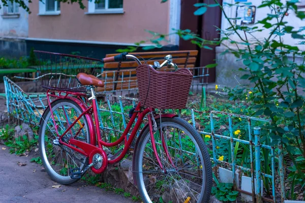 old lady's red bicycle, standing by the fence, against the background of a residential building street Red cottage with mountain bike.