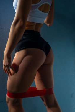 Kusursuz atletik vücudu olan bir bayan sporcunun stüdyo portresi. El germe jimnastik sakızı. Gri arkaplanlı çekici esmer kadın sporcu mükemmel vücutlu, vücudunun üst kısımlarını geliştiren, mavi acti giymiş zayıf kız.