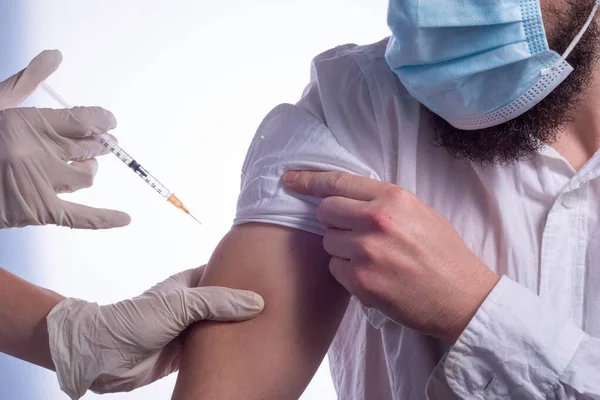 Bir hemşirenin, Coronavirus aşısını maskeli bir hastaya enjekte etmesine karşı aşı. Kişisel koruyucu giysi giymiş beyaz bir doktor ya da koronavirüs enfeksiyonu riski olan kadın hastalara bağışıklık kazandırmak için PPE aşısı vuruyor. Coro.