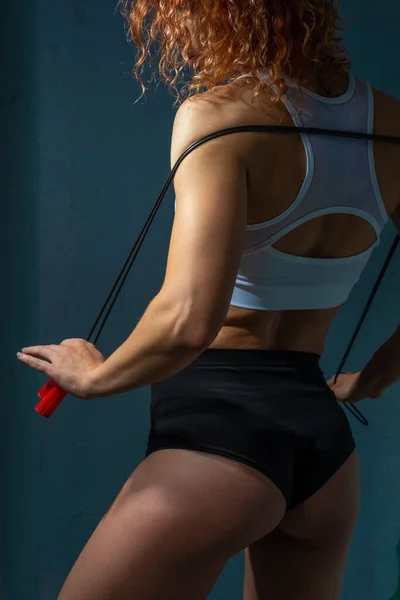 完璧な筋肉や運動体を持つアスリートの女の子 スキップロープを保持します テクスチャブルーの壁の背景に対してポーズ美しいスポーツの女の子は ロープをジャンプして演習を行います — ストック写真
