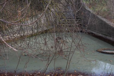 Kanal su kirliliği, çamurlu beyaz suyu olan nehir kanalı, merdivenlerden aşağı akıyor. Fabrikanın kirli sularındaki lastik atık lastikleri.