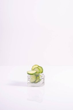 Salatalık bazlı kozmetik. Cam bir kabın içinde dilimlenmiş salatalık halkaları. Beyaz arka planda. minimalizm.