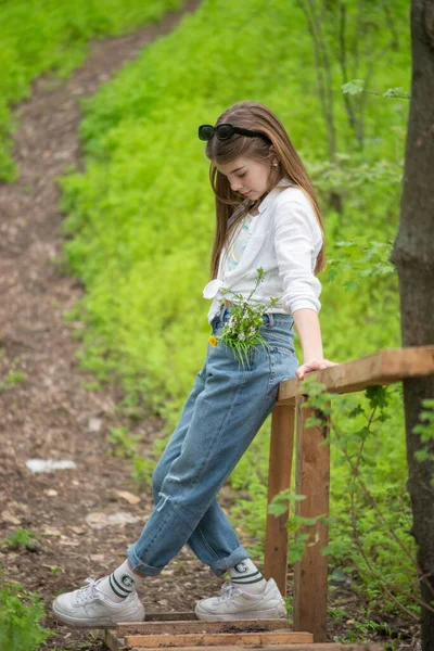 一个时髦小女孩的画像 靠着一座木桥 靠着森林的绿树 — 图库照片