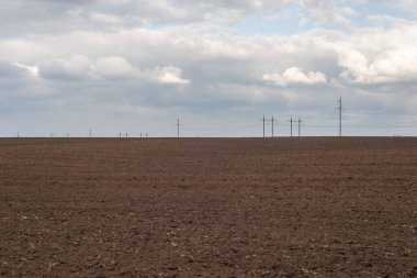 Yüksek voltajlı kulelerin arka planında saban ve bulutların minimalist manzarası
